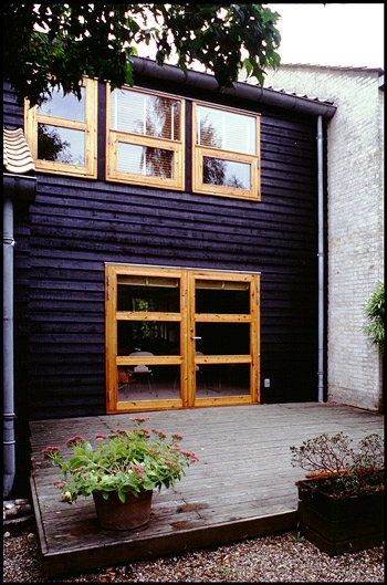 Sjølund Et enkelt rækkehus i to etager med dobbelt havedør ud til den hævede terrasse med plankegulv.
